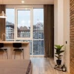 Contemporary apartment interior with bed and kitchen counter and overlooking floor to ceiling window