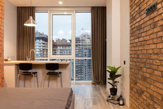 Contemporary apartment interior with bed and kitchen counter and overlooking floor to ceiling window