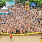 From above people in swimsuits standing together behind line tape ready to start swim marathon on seashore