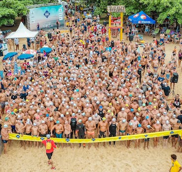 From above people in swimsuits standing together behind line tape ready to start swim marathon on seashore