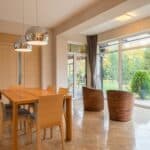 Interior of spacious dining zone with panoramic windows furnished with wooden table and chairs on tilled floor in villa