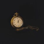 Vintage watch with chain and white dial placed on black background in studio