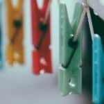 Closeup of small vibrant multi colored clothespins on white thin clothesline in daylight on blurred background