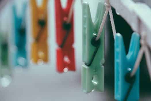 Closeup of small vibrant multi colored clothespins on white thin clothesline in daylight on blurred background