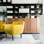 Creative yellow armchairs placed near wooden coffee table in cozy living room with creative shelves decorative houseplants