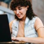 Crop smiling freelancer working on laptop at cafe table outdoors