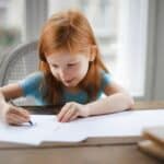 Diligent small girl drawing on paper in light living room at home