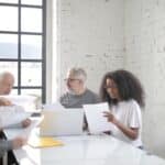 Focused multiracial coworkers of different ages in casual clothes brainstorming on new business ideas and company strategy while sitting at table in creative workspace