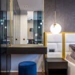 Modern light room interior with mirror with shelf decorated with small potted plants near pouf and lamps near bedside table