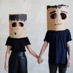 A Couple Wearing Diy Cardboard Box Mask While Holding Each Other's Hands