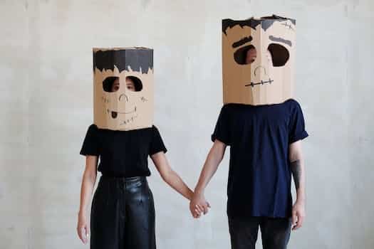 A Couple Wearing Diy Cardboard Box Mask While Holding Each Other's Hands