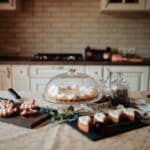 Appetizing sweet cake and desserts decorated with cream and strawberries placed on table near white cabinets in kitchen