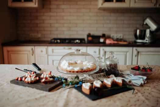 Appetizing sweet cake and desserts decorated with cream and strawberries placed on table near white cabinets in kitchen