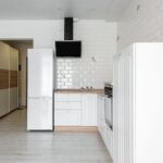 Contemporary kitchen with refrigerator and hood against decorative white brick wall in house with empty shelves on parquet