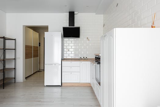 Contemporary kitchen with refrigerator and hood against decorative white brick wall in house with empty shelves on parquet