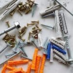 Set of assorted multicolored plastic dowels and various metal screws of different sizes placed on white marble table in workshop