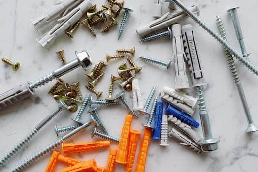 Set of assorted multicolored plastic dowels and various metal screws of different sizes placed on white marble table in workshop