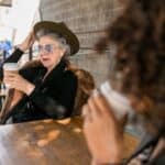 Woman in Black Long Sleeve Shirt Sitting on Chair With Coffee