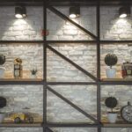 Different clocks with ornament and potted plants on wooden shelves near rough wall illuminated by shiny lamps in house