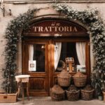 Exterior of cozy Italian restaurant with wooden door and entrance decorated with plants