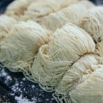 Homemade egg noodles collected in rolls and sprinkled with flour on black baking sheet