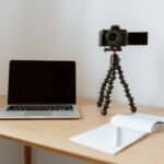 Modern workplace consisting of netbook camera on tripod near opened planner with pen on wooden table