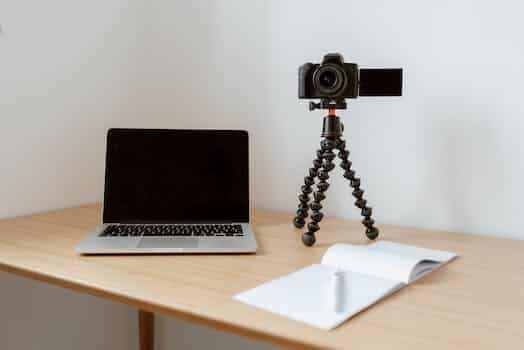 Modern workplace consisting of netbook camera on tripod near opened planner with pen on wooden table