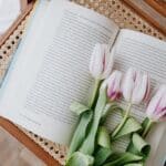 Composition of fresh romantic flowers on open book arranged on vintage wicker table at home