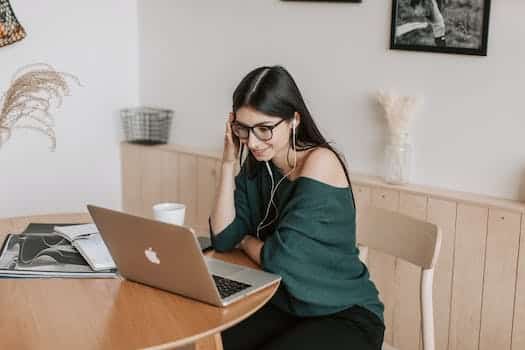 Smiling student in earphones watching laptop at table at home