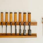 Collection of metal chisels with wooden handles and wood cutters for woodwork arranged on shelf on white wall in workshop