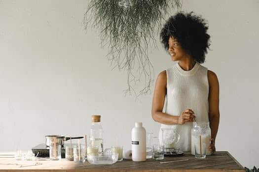 Content African American female artisan with jar of wax flakes looking away while creating candles in modern workshop in light room