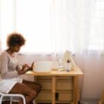 Creative casually dressed female artist painting hand crafted bowl while sitting in cozy workspace