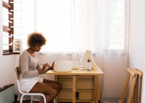 Creative casually dressed female artist painting hand crafted bowl while sitting in cozy workspace