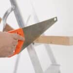 Crop man sawing wooden plank at home