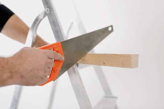 Crop man sawing wooden plank at home