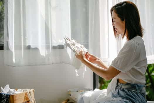 Side view of Asian craftswoman with poles and cotton textile demonstrating Japanese tie dye technique in house on sunny day