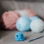 Small soft knitted animal toy with crochet hook and balls of yarn on cozy sofa