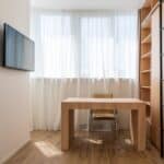 Chair and wooden table placed near window with curtains in home office with TV set