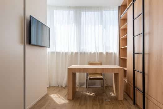 Chair and wooden table placed near window with curtains in home office with TV set