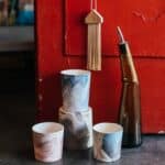 Collection of ceramic pots with creative ornaments near glass bottle placed on floor near shabby red door in modern workshop