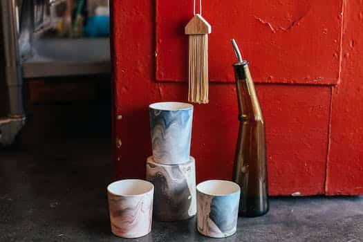 Collection of ceramic pots with creative ornaments near glass bottle placed on floor near shabby red door in modern workshop