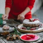 Crop anonymous female in red dress decorating freshly baked delicious pie slice with sugar powder on autumn backyard