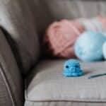 Soft blue crocheted animal toy near hook and yarns on cozy sofa at home