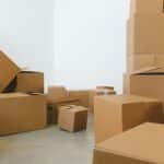 Stack of carton boxes of various shapes and sizes scattered in floor near white walls during relocation