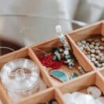 Wooden container with abundance of colorful beads and elastic cord for making bracelet placed on glass table in light room